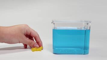 A hand drops pasta into a blue liquid, observing its buoyancy changes in a clear container video