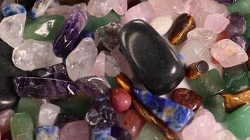 Chakra stones rotate on a vibrant bed of various gemstones, showcasing their colors and textures under soft lighting video