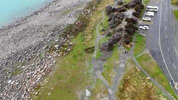 Drone footage captures Lake Tekapo's rocky shoreline and adjacent parking area under natural daylight, showcasing the serene lakeside environment video