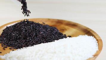 Riceberry grains are poured onto white rice in a wooden bowl, highlighting contrast and texture under soft lighting video