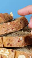 A hand picks a slice of whole wheat bread from a stack, set against a bright blue backdrop video