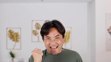 A man expresses excitement with a fist pump in a bright, home environment. Neutral tones and framed art create a cozy atmosphere video