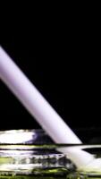 A white rod interacts with liquid, forming soap bubbles in a dark setting with reflective surfaces video