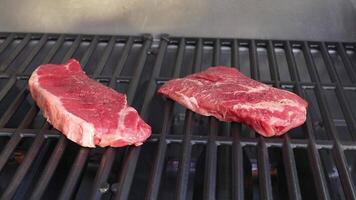 Two beef steaks cooking on a barbecue grill. Close-up view with even lighting and minimal camera movement video