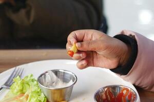 A young hand holds a french fry topped with ketchup while sitting photo