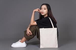 Female Sitting on Floor Holding Blank Canvas Tote Bag, Eco-Friendly Reusable Fabric with Handle, Close-Up Mockup, No Plastic and Environmental Concept Background photo