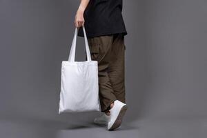 Female Walking While Holding White Canvas Tote Bag, Eco-Friendly Reusable Fabric with Handle, Close-Up Mockup, No Plastic and Environmental Concept photo
