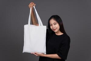 Front View of Woman Holding Blank Canvas Tote Bag, Eco-Friendly Reusable Fabric with Handle, Close-Up Mockup, No Plastic and Environmental Smiling photo