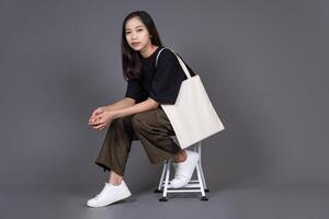 Woman Sitting on Chair Holding Blank Canvas Tote Bag, Eco-Friendly Reusable Fabric with Handle, Close-Up Mockup, No Plastic and Environmental Concept Isolated Background photo