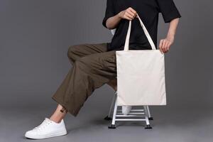 Woman Sitting on Chair Holding Blank Canvas Tote Bag, Eco-Friendly Reusable Fabric with Handle, Close-Up Mockup, No Plastic and Environmental Concept Isolated photo