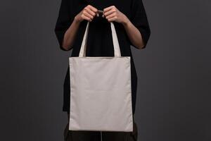 Front View of Woman Holding Blank Canvas Tote Bag, Eco-Friendly Reusable Fabric with Handle, Close-Up Mockup, No Plastic and Environmental Concept Dark Background photo