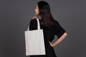 Back View of Woman Holding Blank Canvas Tote Bag, Eco-Friendly Reusable Fabric with Handle, Close-Up Mockup, No Plastic and Environmental Concept photo