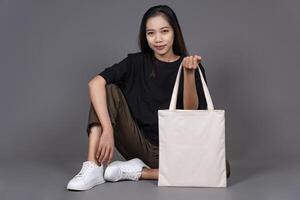 Female Sitting on Floor Holding Blank Canvas Tote Bag, Eco-Friendly Reusable Fabric with Handle, Close-Up Mockup, No Plastic and Environmental Concept photo