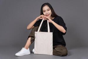 Woman Sitting on Floor Holding Blank Canvas Tote Bag, Eco-Friendly Reusable Fabric with Handle, Close-Up Mockup, No Plastic and Environmental Concept photo