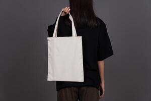 Back View of Woman Holding Blank Canvas Tote Bag, Eco-Friendly Reusable Fabric with Handle, Close-Up Mockup, No Plastic and Environmental Concept Isolated Background photo