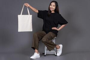 Female Sitting on Chair Holding Blank Canvas Tote Bag, Eco-Friendly Reusable Fabric with Handle, Close-Up Mockup, No Plastic and Environmental Concept photo