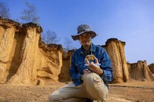 Asian geologist is exploring and surveying the sample rock on the natural sandstone canyon quarry site for scientific research and archeology for understanding earth photo