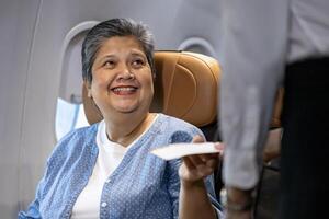 Flight attendant is welcoming and checking senior woman passenger boarding pass and show her seat for airplane flight and airline business photo