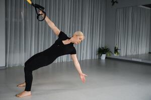 Fitness enthusiast performs suspension training exercise in a spacious studio with natural lighting during a workout session focused on strength and balance photo