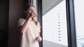 young woman enjoying drinking tea in the hotel room in the morning , looking to the window enjoying the view video