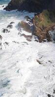 Powerful ocean waves crash against rocky cliffs under bright sunlight, creating a dynamic and dramatic coastal scene video
