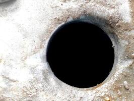 Close-up of a dark circular hole in a rough, textured surface. photo