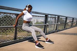 Young African-American woman doing reverse push-ups outdoors on a city bridge, showing strength and focus during her workout routine. photo