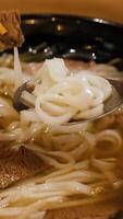 Chopsticks and spoon interact with steaming pho noodles and beef in a warm, inviting setting video