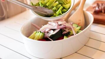 A vibrant salad is assembled with fresh vegetables using tongs in a bright kitchen setting video