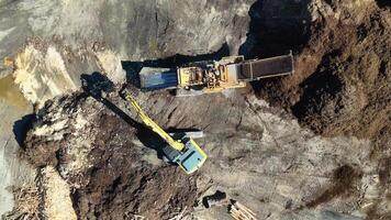 Drone footage captures an excavator moving mulch in a dirt processing area under bright sunlight video
