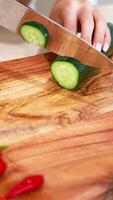 Hands slicing cucumber on a wooden board in a bright kitchen. Natural lighting enhances the fresh, vibrant atmosphere video