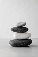 A zen stack of four smooth stones in varying shades of gray against a white background photo