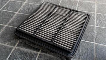 Top view of old engine air filter of car. Cloth panels are covered with black dust. Placed on a black tiled floor. photo