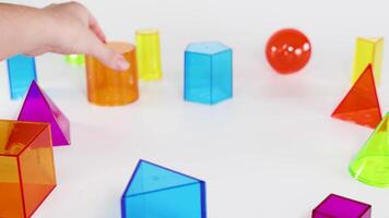 Hands stack colorful 3D geometric shapes on a table, demonstrating balance and coordination in a well-lit environment video