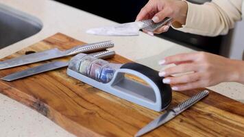 A person sharpens a knife using a handheld sharpener on a wooden board in a well-lit kitchen video