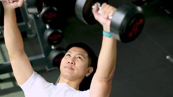 A man exercises with dumbbells on a bench in a well-lit gym, focusing on strength training video