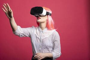 Caucasian female model using VR headset reaching forward with her hand, engaging with futuristic digital world. Young lady in virtual reality gear, immersed in advanced 3D simulation. photo