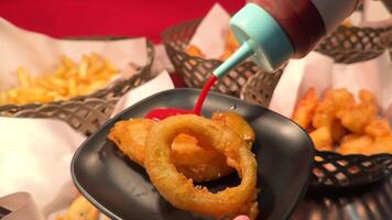 Close-up of sauces being poured on fried onion rings in a vibrant restaurant setting with fries and shrimp video