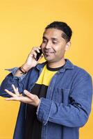 A friendly person with man bun calling his friend on phone call to gossip, sharing information in a remote conversation against studio background. Indian cheerful man with a modern lifestyle. photo