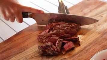 A person slices a cooked beef steak on a wooden board in a well-lit kitchen setting video