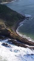 Aerial footage captures the dynamic coastline of Byron Bay with crashing waves and lush greenery under bright sunlight video
