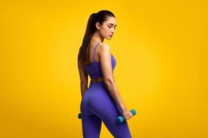 Fitness Model. Portrait Of Confident Young Woman Exercising With Two Dumbbells Posing Isolated Over Orange Background, Turning Back And Looking Down. Studio Shot, Free Space, Banner photo