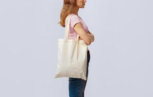 Side View Shot Of Young Woman Carrying Blank Eco Tote Canvas Bag, Unrecognizable Millennial Lady Enjoying Sustainable Shopping, Standing Over Light Studio Background, Cropped Image, Copy Space photo