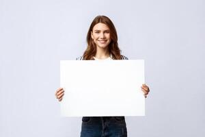 Smiling Millennial Lady Holding Blank Placard With Copy Space For Advertisement. Positive Young Woman Showing Empty Poster With Free Place For Your Text Or Design, Standing On Light Studio Background photo
