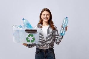 Waste Sorting. Smiling Eco Volunteer Woman Holding Container With Empty Plastic Bottles, Cheerful Lady Promoting Garbage Recycling Concept While Posing Over Gray Studio Background, Free Space photo