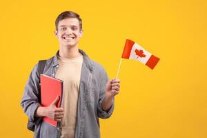 Canada day, patriotism and knowledge sharing. Millennial smiling european guy in casual with backpack, notepads and small flag, isolated on orange background, cut out, copy space, studio shot photo