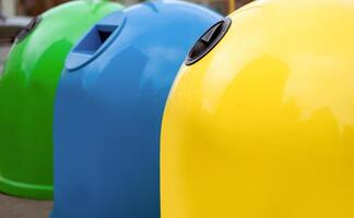 Waste Sorting Concept. Closeup Shot Of Colorful Garbage Containers For Different Sort Of Materials Standing Outdoors, Yellow Blue And Green Trash Bin For Diverse Kind Of Trash For Recycling photo