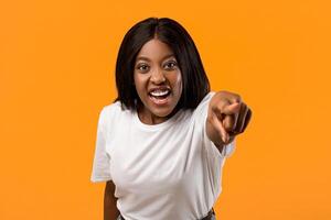 Angry black lady yelling and pointing at camera, orange studio background, closeup portrait. Furious african american young woman shrieking, feeling irritated. Negative emotions, anger concept photo