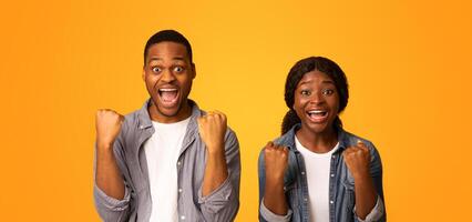 Unbelievable Success. Portrait Of Euphoric African American Couple Standing With Open Mouth And Raised Fists, Excited Black Man And Woman Standing Isolated On Yellow Background, Free Space photo