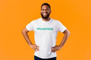 Cheerful African Volunteer Guy Standing With His Hands On Hips Ready For Voluntary Work Posing On Yellow Studio Background, Smiling To Camera. Volunteering Job, Activist's Portrait Concept photo